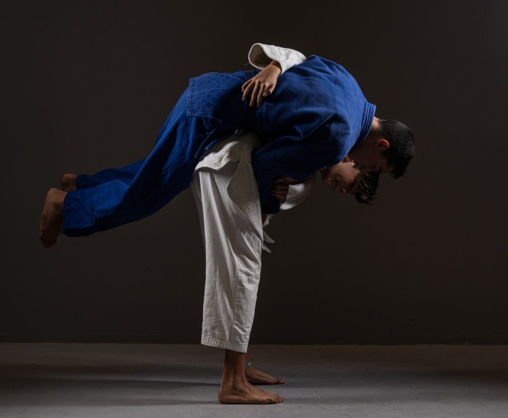 Side view of young barefooted Asian male judokas in uniform fighting on floor against black background